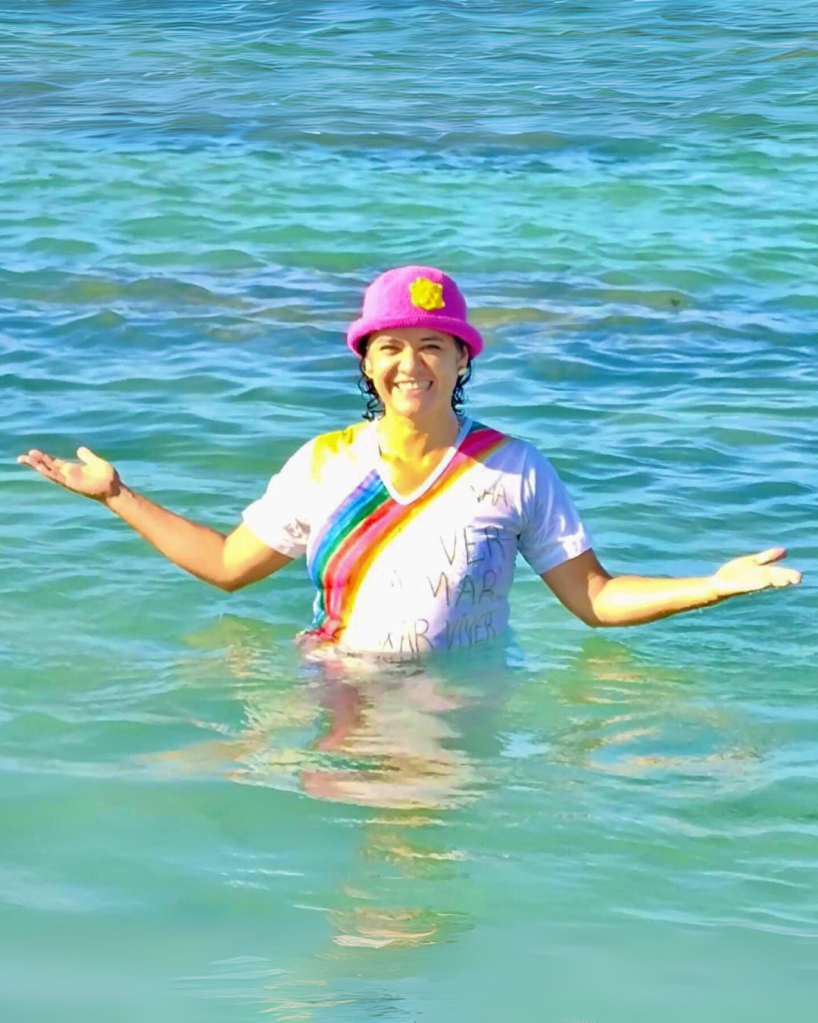 Mulher dentro do mar de braços abertos sorrindo.